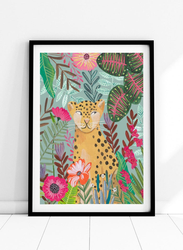 Illustration of a cheetah surrounded by colorful flowers and leaves on a light blue background. Happy Leopard Tropical Flowers by Caroline Bonne Müller is a fine art print and wall poster featuring a leopard with tropical flowers in a modern aesthetic style.