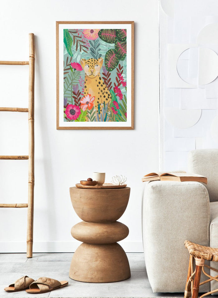 Illustration of a cheetah surrounded by colorful flowers and leaves on a light blue background. Happy Leopard Tropical Flowers by Caroline Bonne Müller is a fine art print and wall poster featuring a leopard with tropical flowers in a modern aesthetic style.