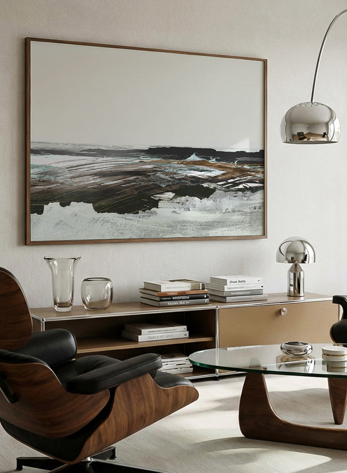 A framed abstract landscape art print featuring textured brushstrokes of brown, white, gray, and black. Shop Constantine Bay by Dan Hobday, a contemporary coastal wall art print with abstract shoreline forms, pale blue accents, dark brown tones, and textured brushwork.