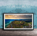 The image is a framed aerial view of a mountainous landscape with a coastal area, featuring a mix of green, brown, and blue colors.