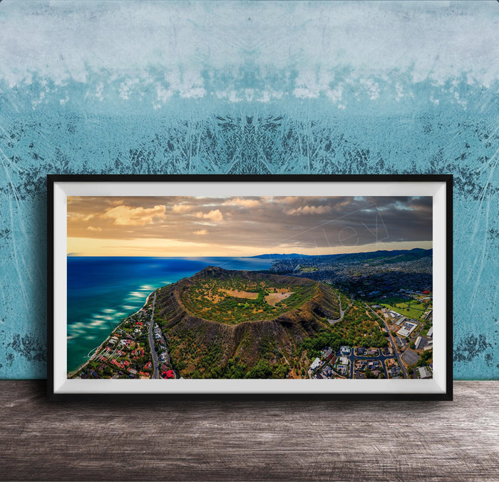 The image is a framed aerial view of a mountainous landscape with a coastal area, featuring a mix of green, brown, and blue colors.