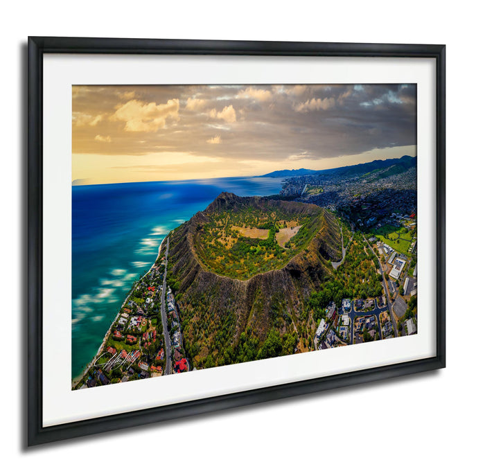 The image is a framed aerial view of a mountainous landscape with a coastal area, featuring a large hill or mountain peak surrounded by lush greenery and a body of water.