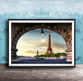 A framed photograph of the Eiffel Tower in Paris, France, with the tower visible through an archway. The sky is blue with clouds, and the sun is setting, creating a picturesque scene.