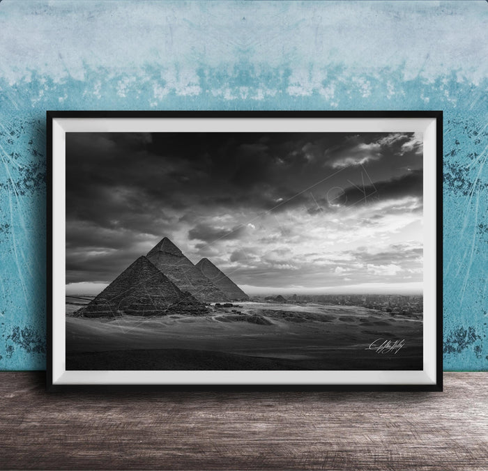 A black and white photograph of the iconic pyramids of Giza in Egypt, set against a dramatic cloudy sky.