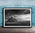 A black and white photograph of the iconic pyramids of Giza in Egypt, set against a dramatic cloudy sky.