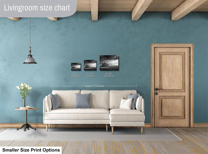 a living room with a white sofa, a wooden door, and a hanging light fixture. There are three framed black and white landscape paintings on the wall, each with different sizes and dimensions. The living room appears to be designed for a smaller, more intimate space.