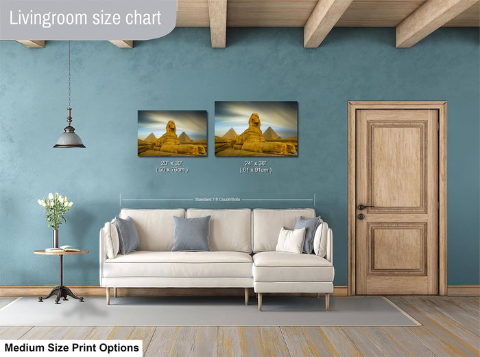 a living room with a white sofa and a wooden door. Above the sofa, there is a size chart for a painting of the pyramids of Giza, indicating the dimensions of the artwork in both centimeters and inches.
