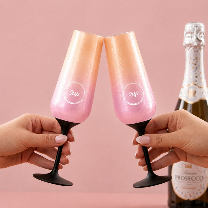 two insulated champagne flutes in an ombre lover colour celebrating with a cheers and bottle of prosecco