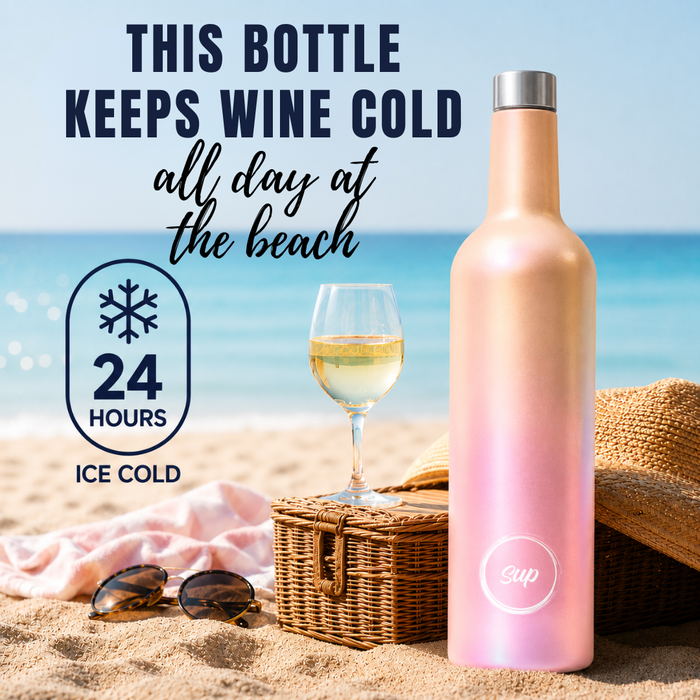 A wine bottle-shaped water bottle with a pink-to-rose gold iridescent finish stands on a sandy beach next to a picnic basket, sunglasses, a drink in a glass, and a straw hat. Text on the image says the bottle keeps wine cold all day at the beach, with a 24-hour ice-cold badge.