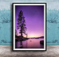 A framed photograph of a serene landscape at sunset, featuring a silhouetted tree against a vibrant purple and orange sky, with calm water in the foreground.