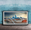 A framed photograph of a city skyline with a large bridge spanning a river, set against a blue sky with clouds.