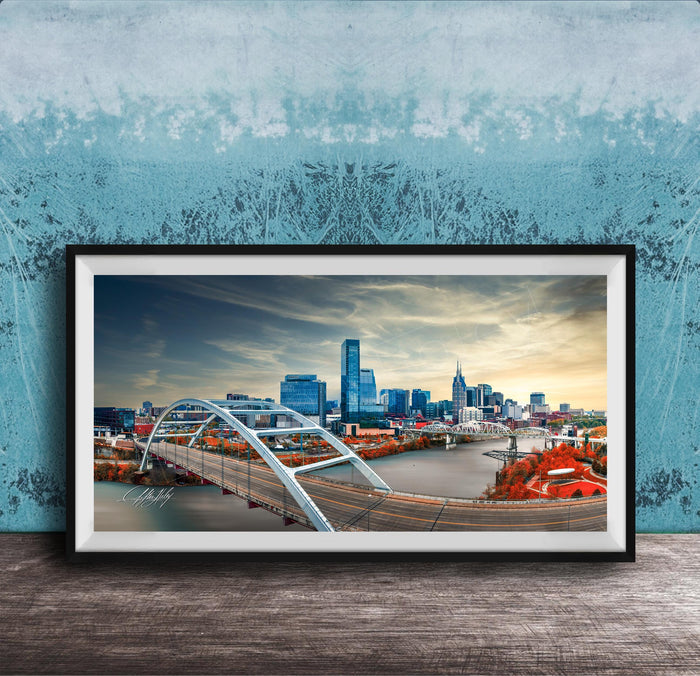 A framed photograph of a city skyline with a large bridge spanning a river, set against a blue sky with clouds.