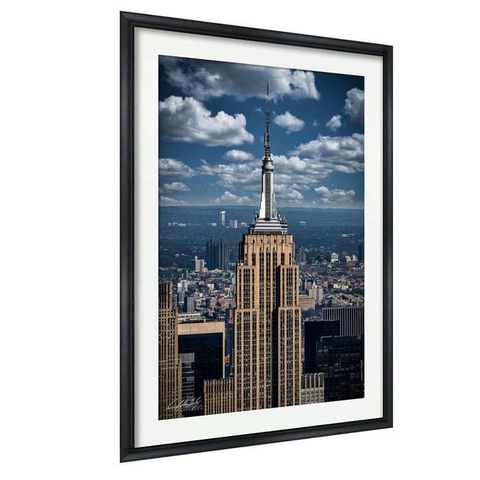 the iconic Empire State Building, a famous skyscraper in New York City, with its distinctive spire and towering presence against a backdrop of a cloudy blue sky.