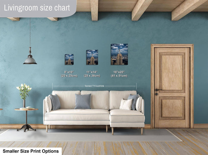 a living room with a white sofa, a wooden door, and a hanging light fixture. There are three framed pictures of cityscapes on the wall, each with a different size and height. The wall is painted in a light blue color, and the floor is made of wood.
