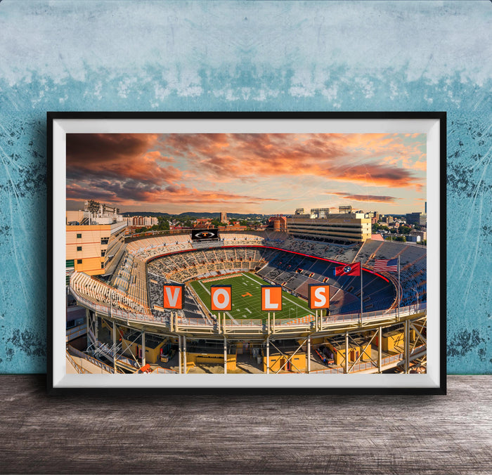 A framed photograph of a sports stadium with the word "VOLS" prominently displayed, set against a backdrop of a colorful sunset sky.