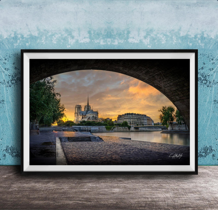 a serene cityscape at sunset, with a large cathedral in the background and a stone bridge arching over a river. The sky is filled with warm, golden hues, creating a picturesque and tranquil atmosphere.