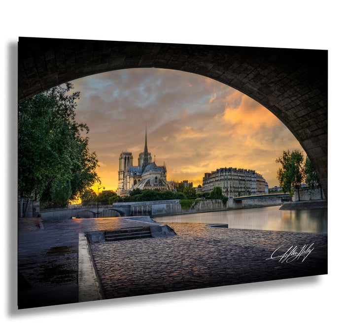 a serene cityscape with a large cathedral in the background, set against a vibrant orange and blue sky at sunset. The cathedral is framed by a stone archway, adding a sense of grandeur to the scene. The photograph is taken from a low angle, emphasizing the height of the cathedral and the archway. The overall composition is visually striking and evokes a sense of tranquility and beauty.