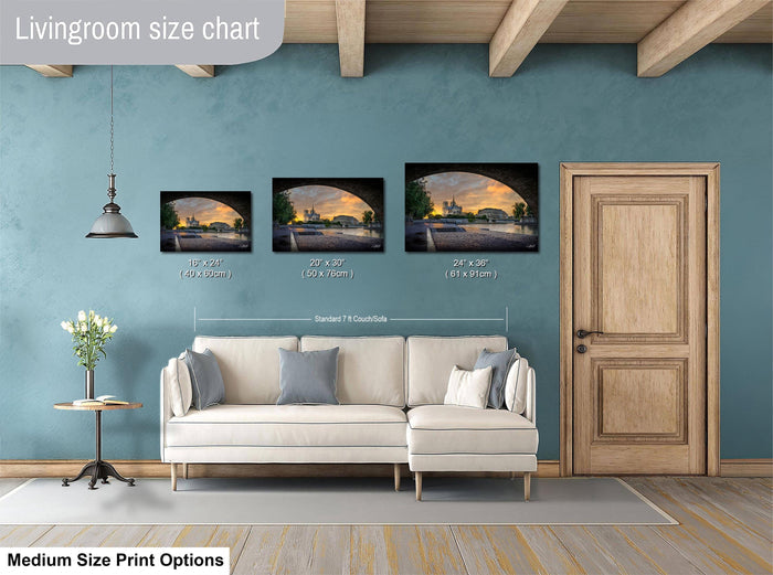 a living room with a white sofa and a wooden door. There are three framed pictures of a sunset displayed on the wall above the sofa. The wall has a blue color, and the floor is made of wood.