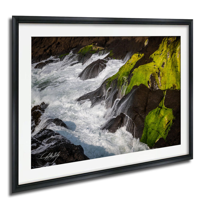 A framed photograph depicting a rocky coastline with flowing water and patches of green moss.