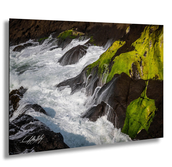 A dramatic landscape featuring a powerful river with white, frothy water flowing over moss-covered rocks.