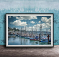 A framed photograph of a harbor with numerous sailboats docked in the water, set against a backdrop of a cloudy sky.