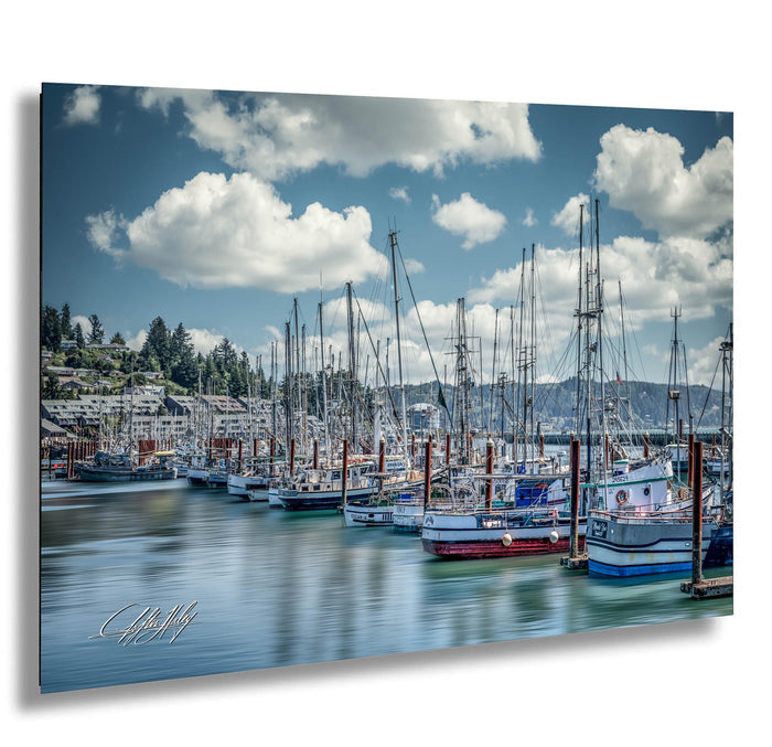 A row of sailboats docked in a harbor, with a backdrop of mountains and a partly cloudy sky.