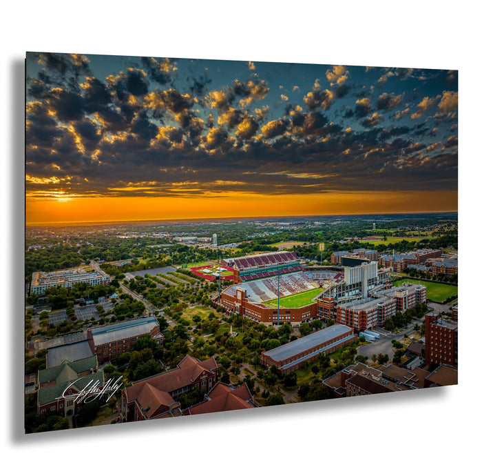 The image is an aerial view of a large sports stadium surrounded by a cityscape, with a dramatic sky in the background.