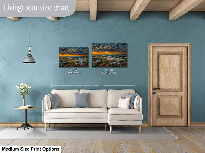 a living room with a white sofa, a wooden door, and a painting of a sunset on the wall. The painting is of a cityscape with buildings and a river. The sofa is positioned in front of the painting, and there is a lamp hanging from the ceiling. The wall has a blue color, and the floor is covered with a rug.