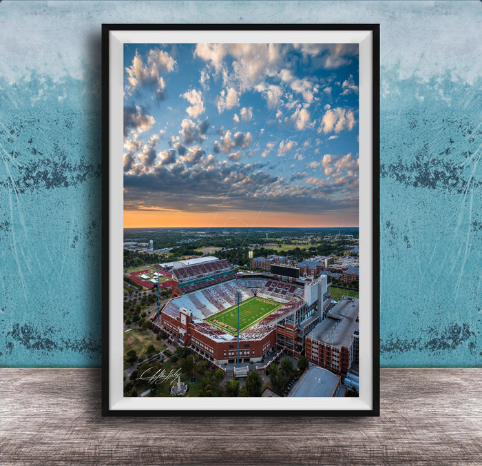 The image is an aerial view of a large sports stadium with a football field, surrounded by buildings and a cloudy sky.