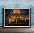 A framed photograph of the Eiffel Tower at night, with the tower illuminated and surrounded by trees and a bridge.