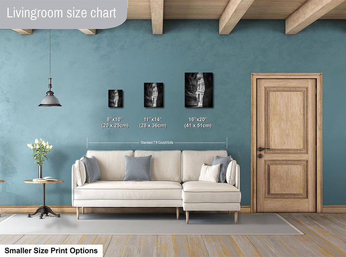 a living room with a white sofa, a wooden door, and a hanging light fixture. There are three framed black and white photographs of people displayed on the wall, each with a different size and height. The wall is painted in a light blue color, and the floor is covered with a gray rug.