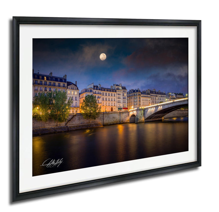 a serene night scene of a cityscape with a full moon, a bridge, and buildings illuminated by warm lights.