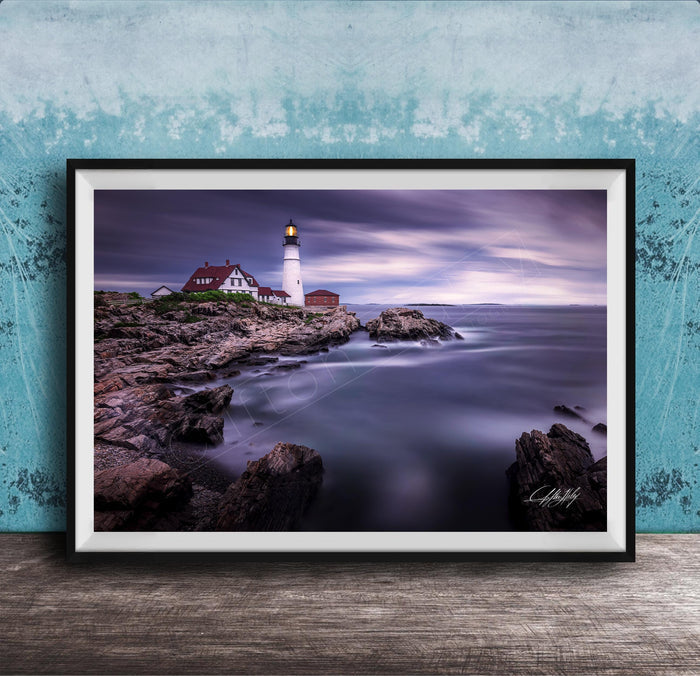 A framed photograph of a lighthouse on a rocky shore, with the ocean and a cloudy sky in the background.