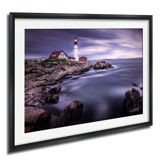 A framed photograph depicting a lighthouse on a rocky shore, with the ocean in the background.