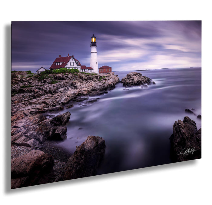 A picturesque lighthouse stands on a rocky shore, overlooking the calm, misty ocean under a dramatic sky.