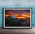 A framed photograph depicting a lighthouse on a rocky cliff at sunset, with the sky filled with vibrant orange and red hues.
