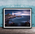 A framed photograph depicting a lighthouse on a rocky coastline, with the ocean and a cloudy sky in the background.