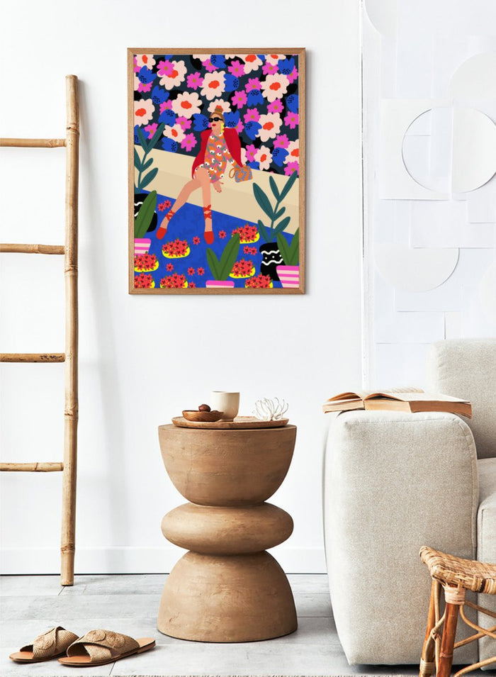 Colorful illustration of a woman sitting on a bench with floral and plant patterns. Bold and Blooming by Rafaela Mascaro fine art print poster featuring woman in vibrant floral garden by water, modern contemporary botanical wall art.