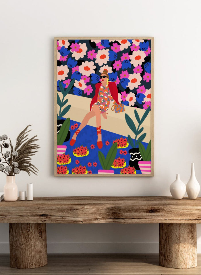 Colorful illustration of a woman sitting on a bench with floral and plant patterns. Bold and Blooming by Rafaela Mascaro fine art print poster featuring woman in vibrant floral garden by water, modern contemporary botanical wall art.