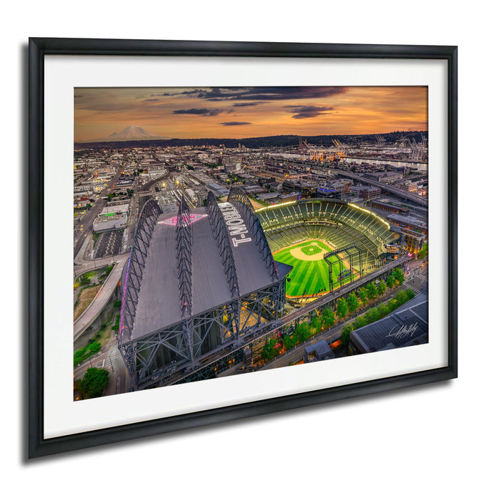 The image is an aerial view of a baseball stadium with a large field and surrounding cityscape at sunset.