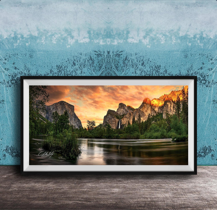 A framed photograph of a scenic mountain landscape at sunset, with a river flowing through the foreground and a waterfall cascading down the mountainside.